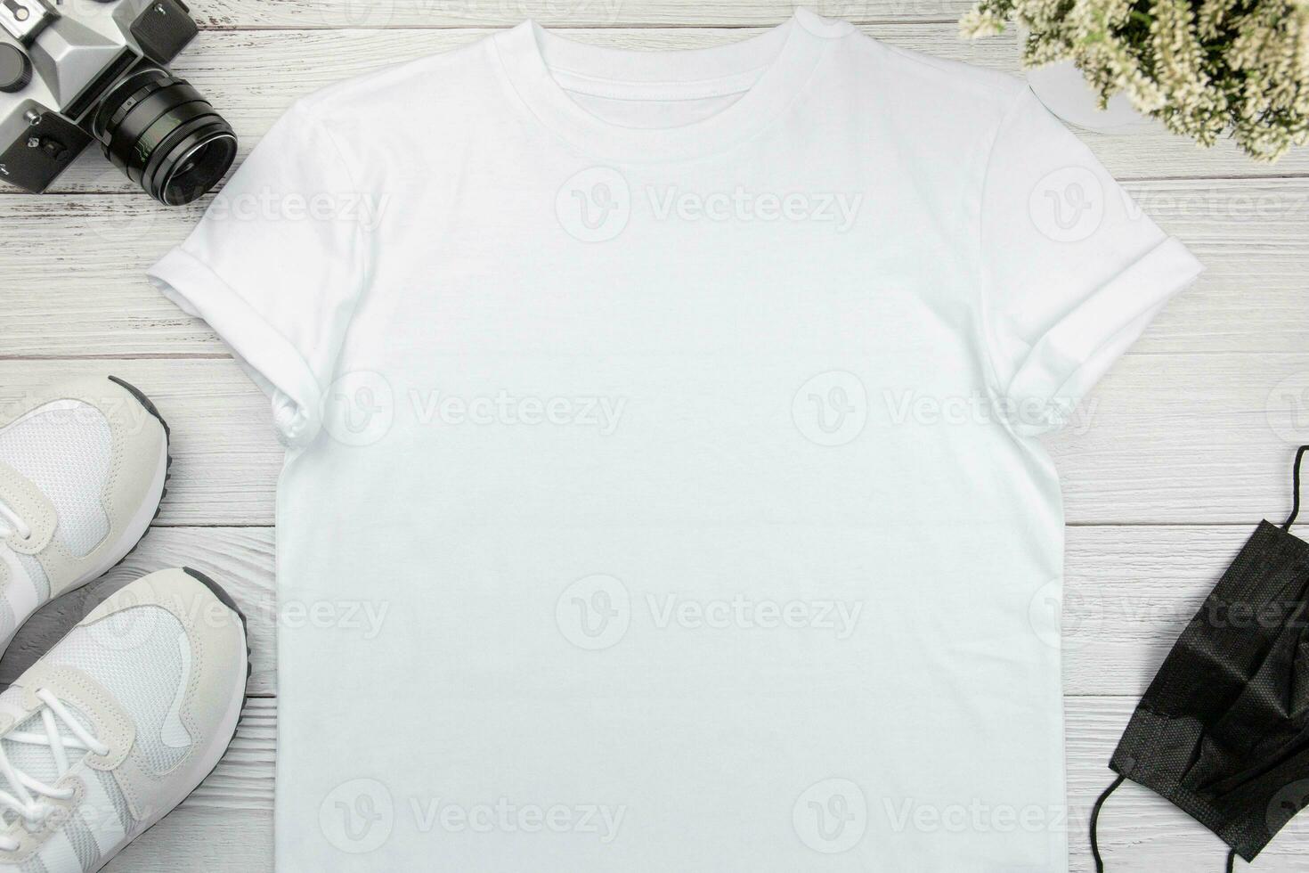 White womens cotton t-shirt mockup with sneaker, retro camera and face mask on white wooden background. Design t shirt template, print presentation mock up. Top view flat lay. photo