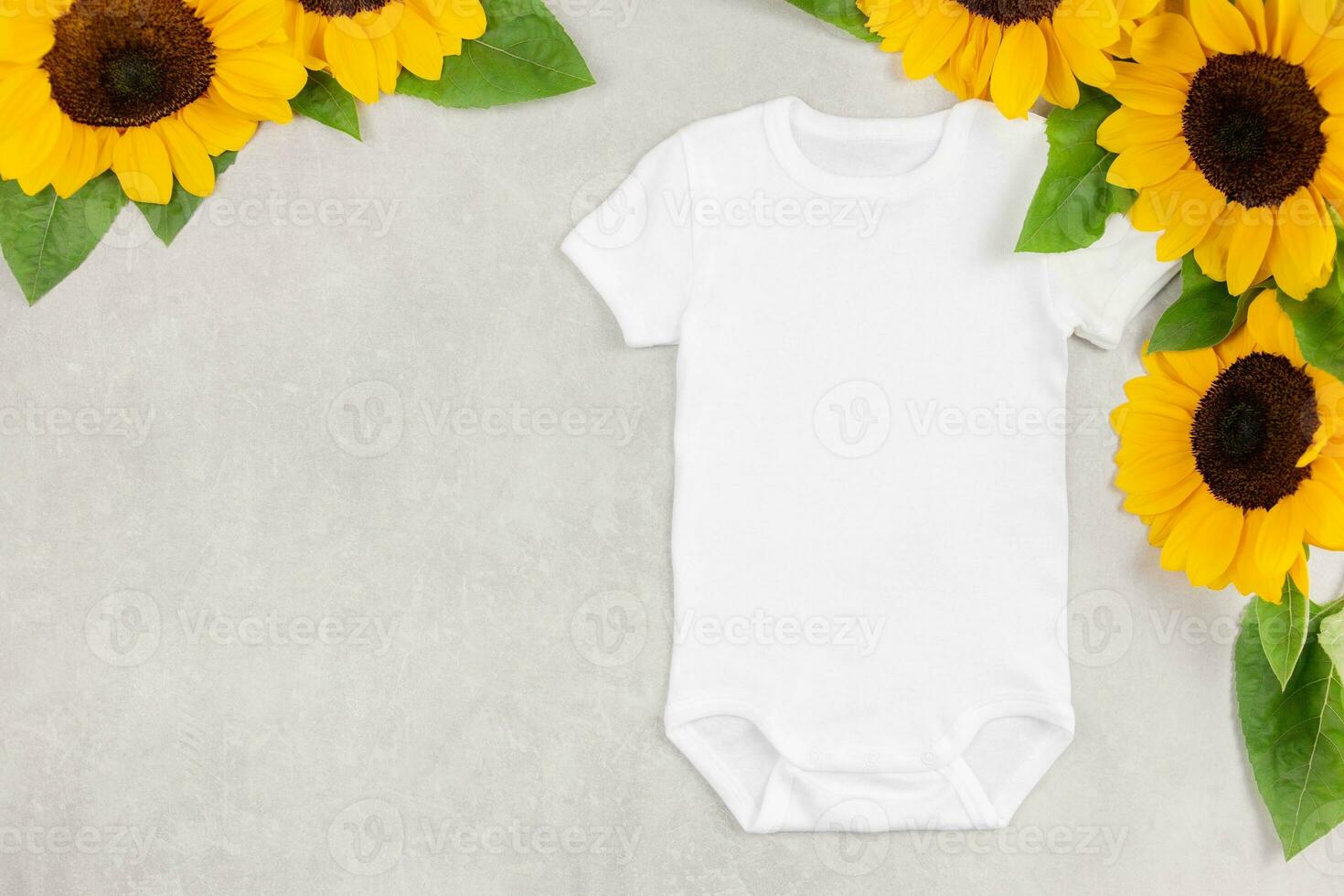 White baby girl or boy bodysuit mockup flat lay with sunflowers on gray concrete background. Design onesie template, print presentation mock up. Top view. photo