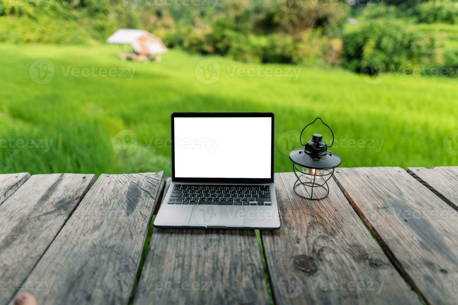 Laptop computer blank screen on a wooden terrace in the background of rice fields photo