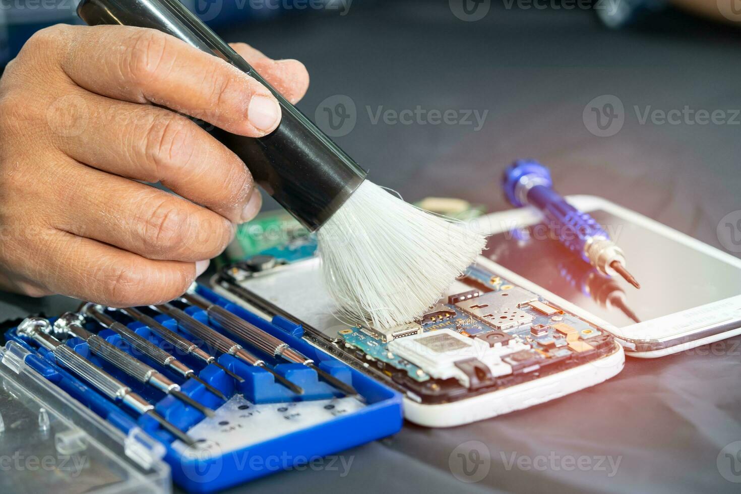 Asian technician repair and cleaning dirty micro circuit main board of smartphone electronic technology with brush, hardware, mobile phone, upgrade concept. photo