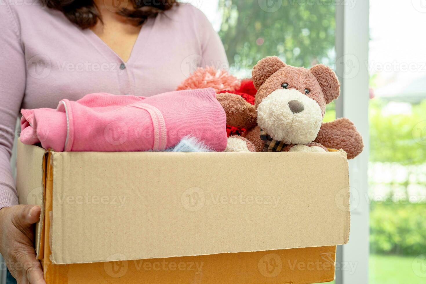 Holding clothing donation box with used clothes and doll at home to support help for poor people in the world. photo