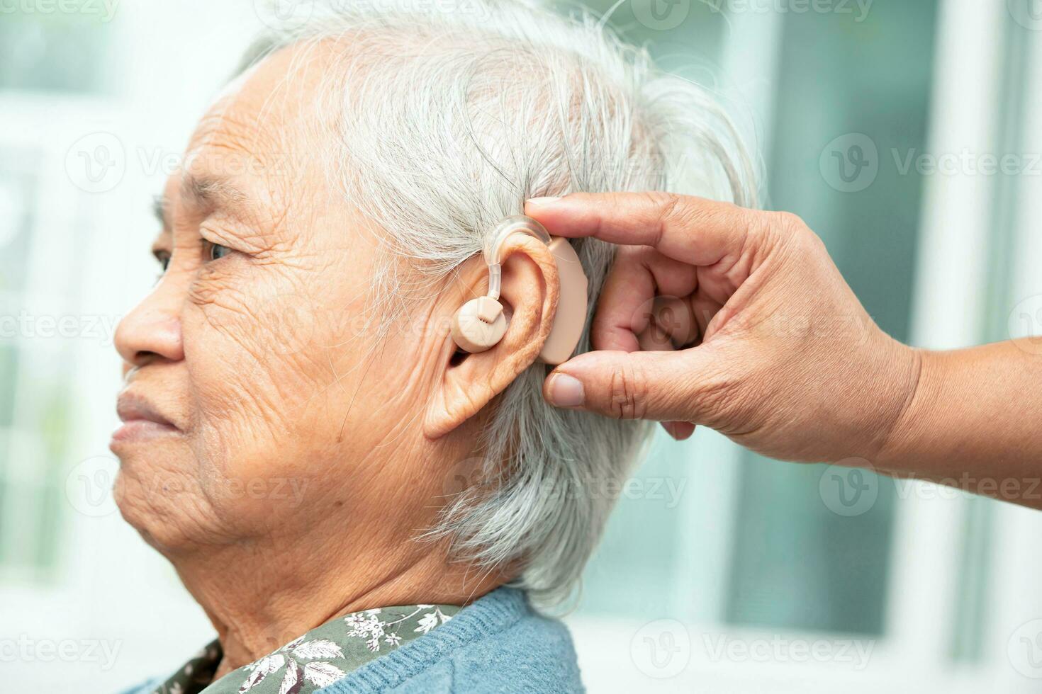 asiático mayor mujer paciente vistiendo un escuchando ayuda para tratando escuchando pérdida problema. foto