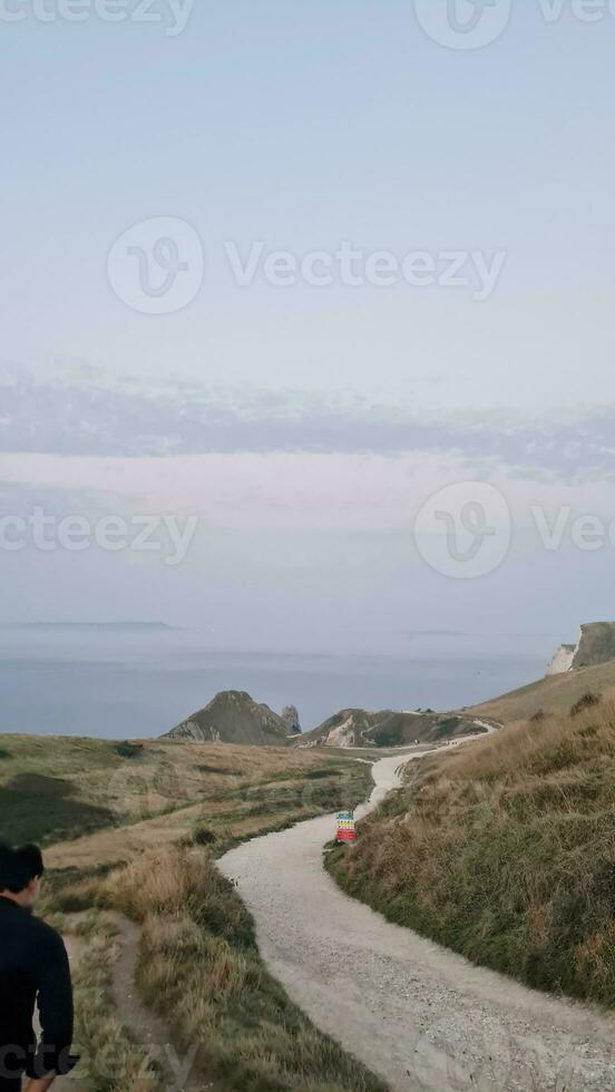 alto ángulo ver de personas son que se acerca a durdle puerta playa cuales es más famoso turista atracción sitio mediante caminando distancia terminado paisaje y sierras. capturado en septiembre 9, 2023 foto