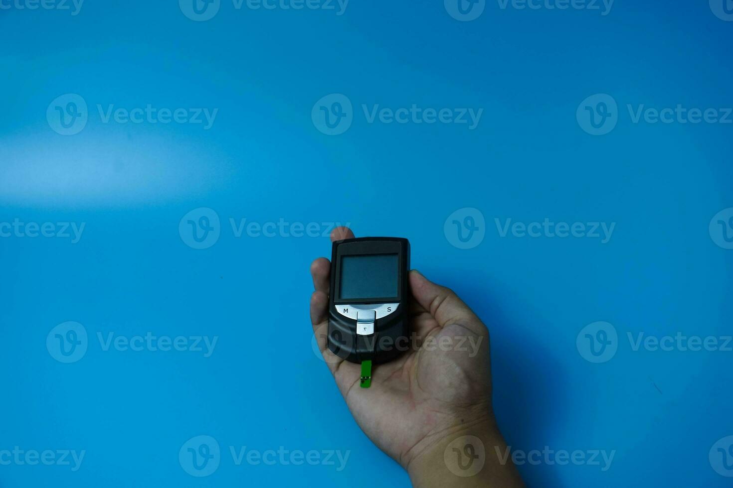 Man checking blood sugar level using glucometer. Diabetes concept on blue background photo