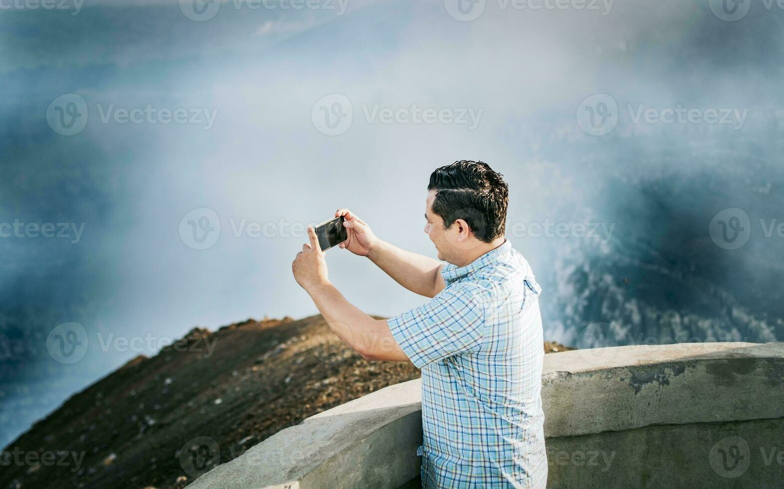 Young tourist man taking photos at a volcanic viewpoint. Adventurous man with his cell phone taking photos at a viewpoint, Tourist man taking photos at a viewpoint