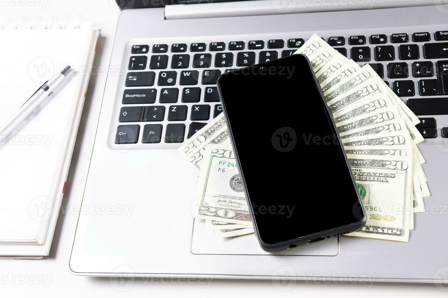 Mobile phone on top of dollar bills on laptop keyboard. Top view of laptop with cell phone and dollar bills. Cell phone on laptop keyboard and dollar bills photo