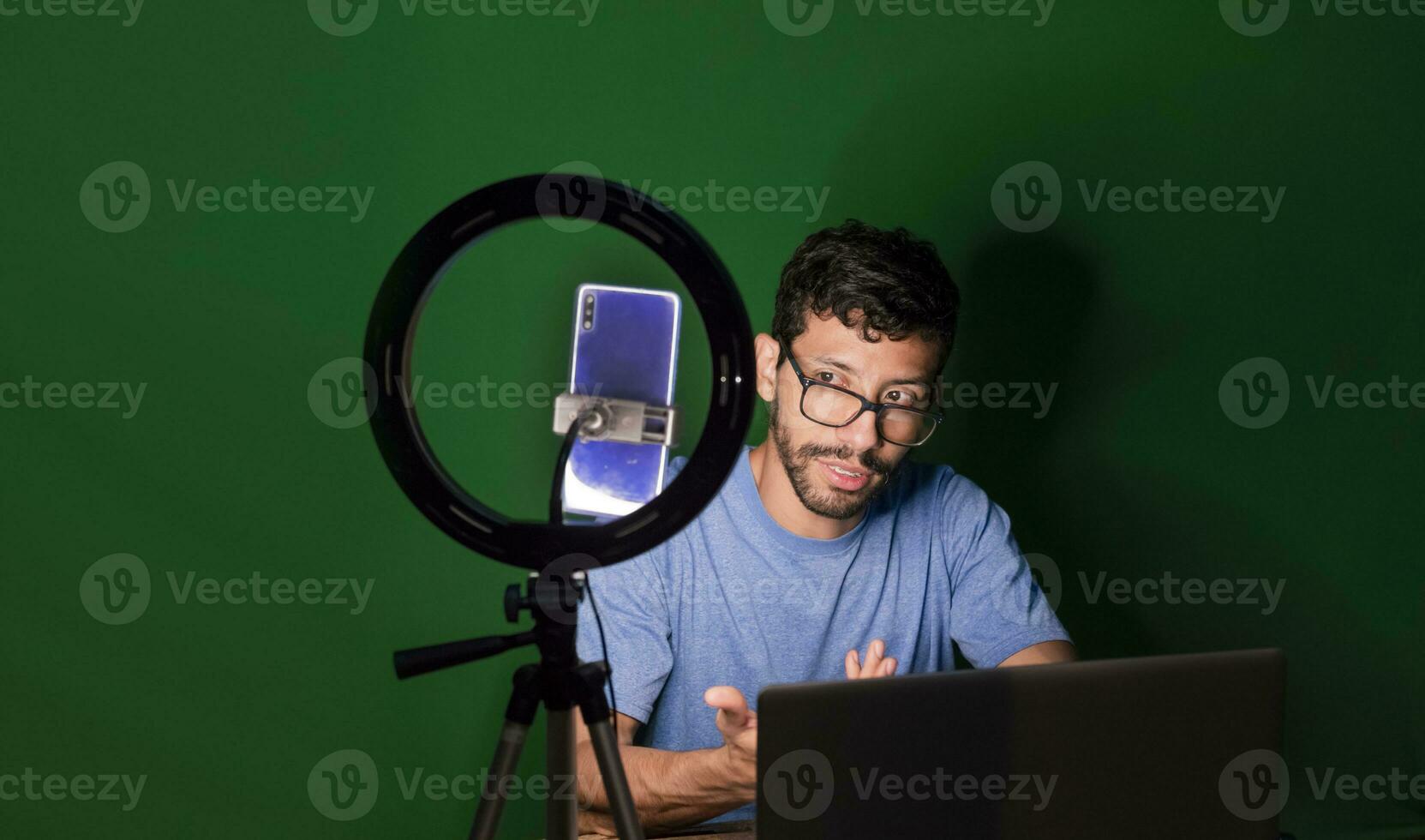 Guy with laptop making video blog on phone. Isolated person giving online classes. Man giving online classes with phone. Guy on a video call working from home. Online classes concept photo