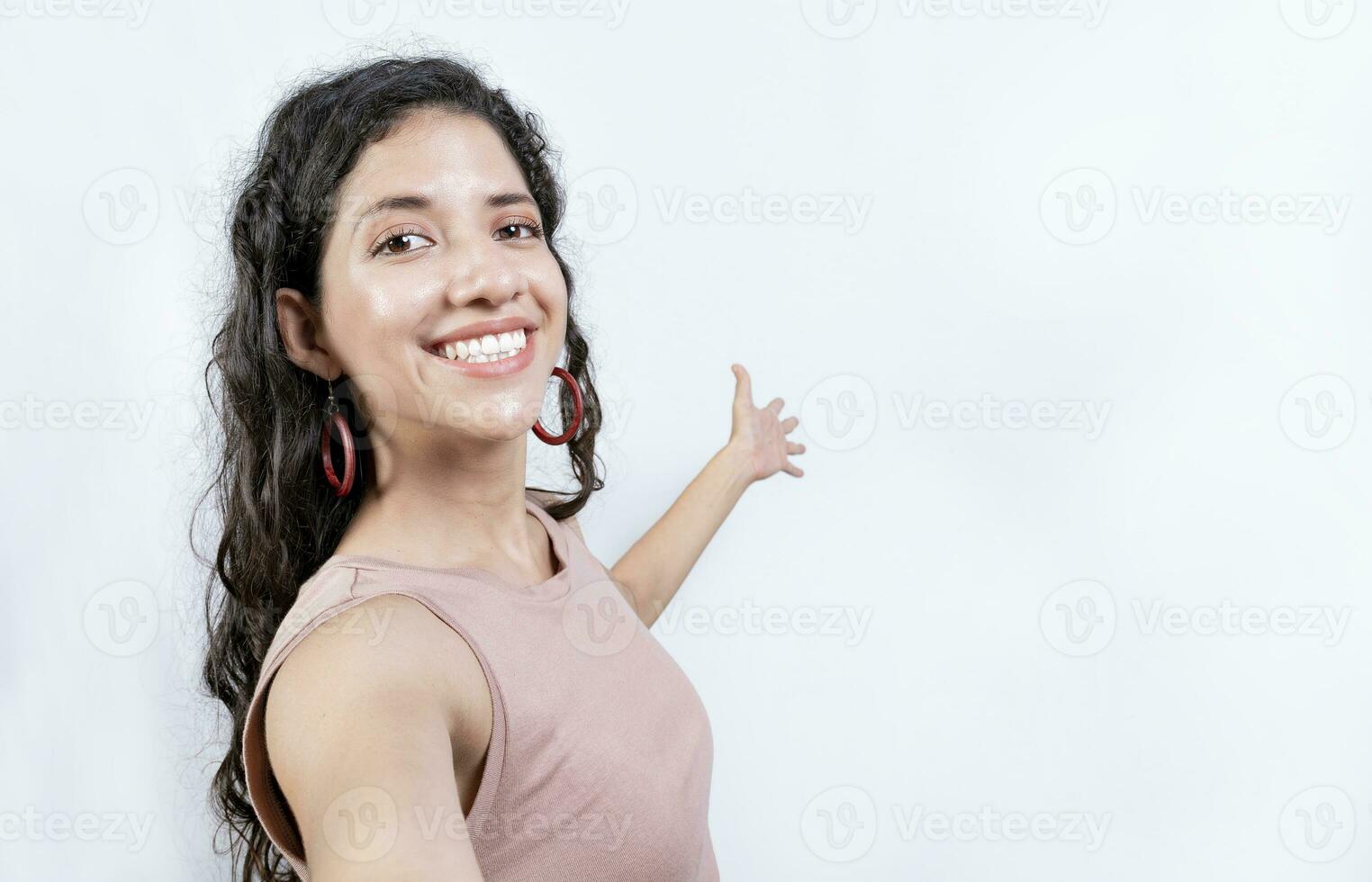 Happy Girl pointing back presenting a product. Young woman welcoming you isolated. Latin girl pointing a promotion with her palm photo