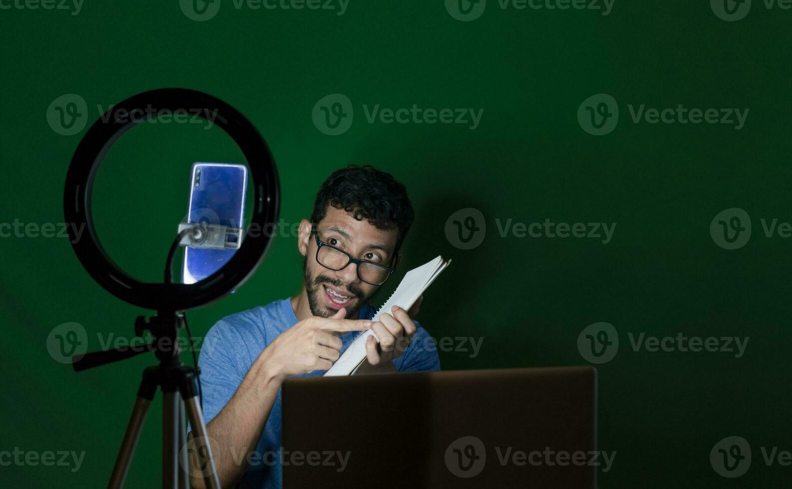 persona dando clases en un vídeo llamar. hombre dando en línea clases con teléfono. chico con ordenador portátil haciendo vídeo Blog en teléfono. chico en un vídeo llamada trabajando desde hogar. en línea clases concepto foto