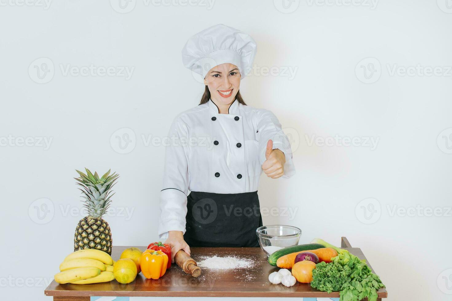 Chef woman holding bread rolling pin with thumb up, Smiling chef woman holding rolling pin on vegetable table, Concept of chef woman holding bread rolling pin photo