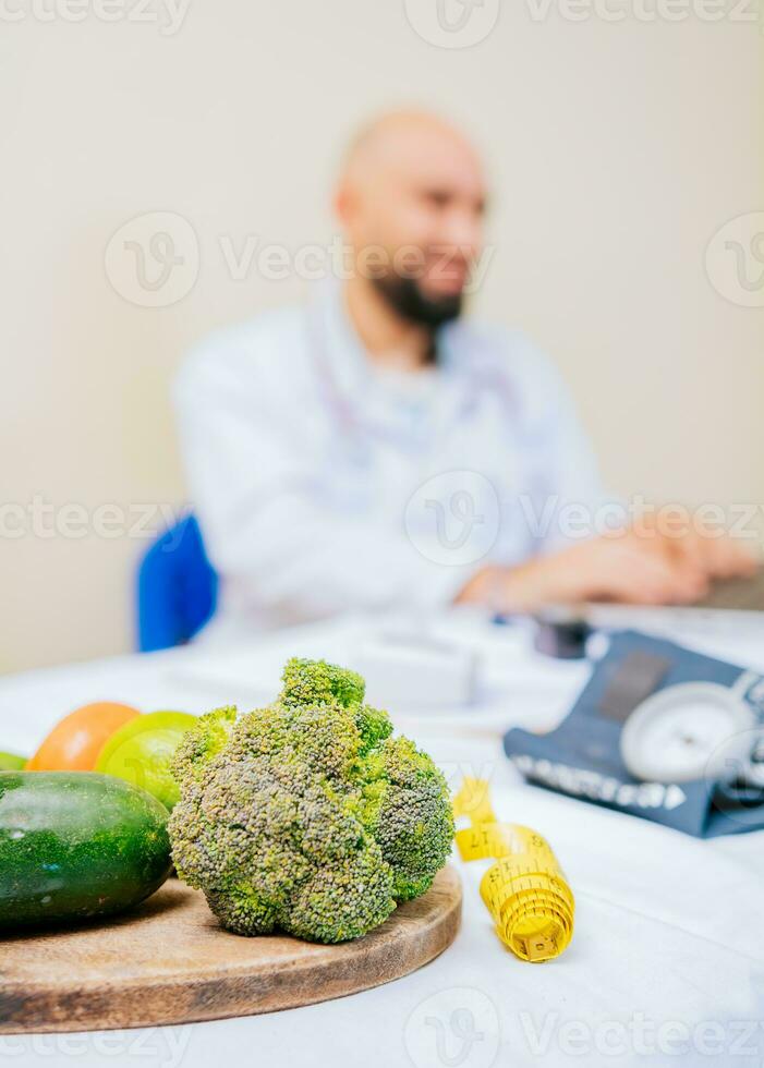 Focus on vegetables of nutritionist with laptop at the desk. Nutritionist working on laptop, giving online consultation to client at clinic, focus on vegetables photo