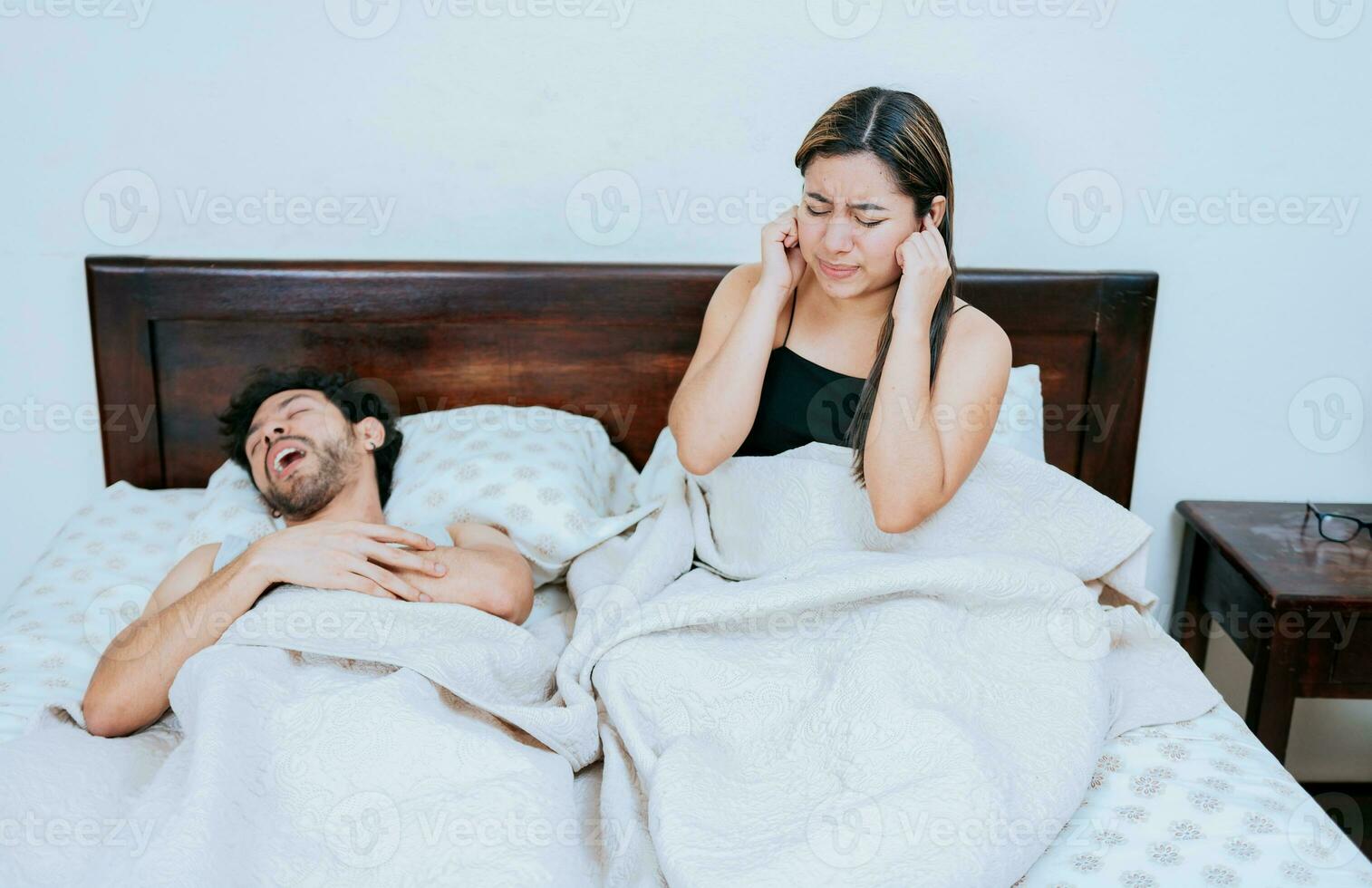 marido ronquidos mientras el esposa sufre y cubre su orejas. dormir apnea concepto, ronquidos hombre en dormitorio y esposa cubierta su orejas foto