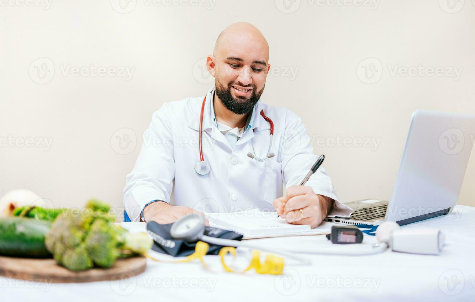 Smiling nutritionist writing in the office. Nutritionist writing on notepad. Male nutritionist working with notes and laptop at desk photo