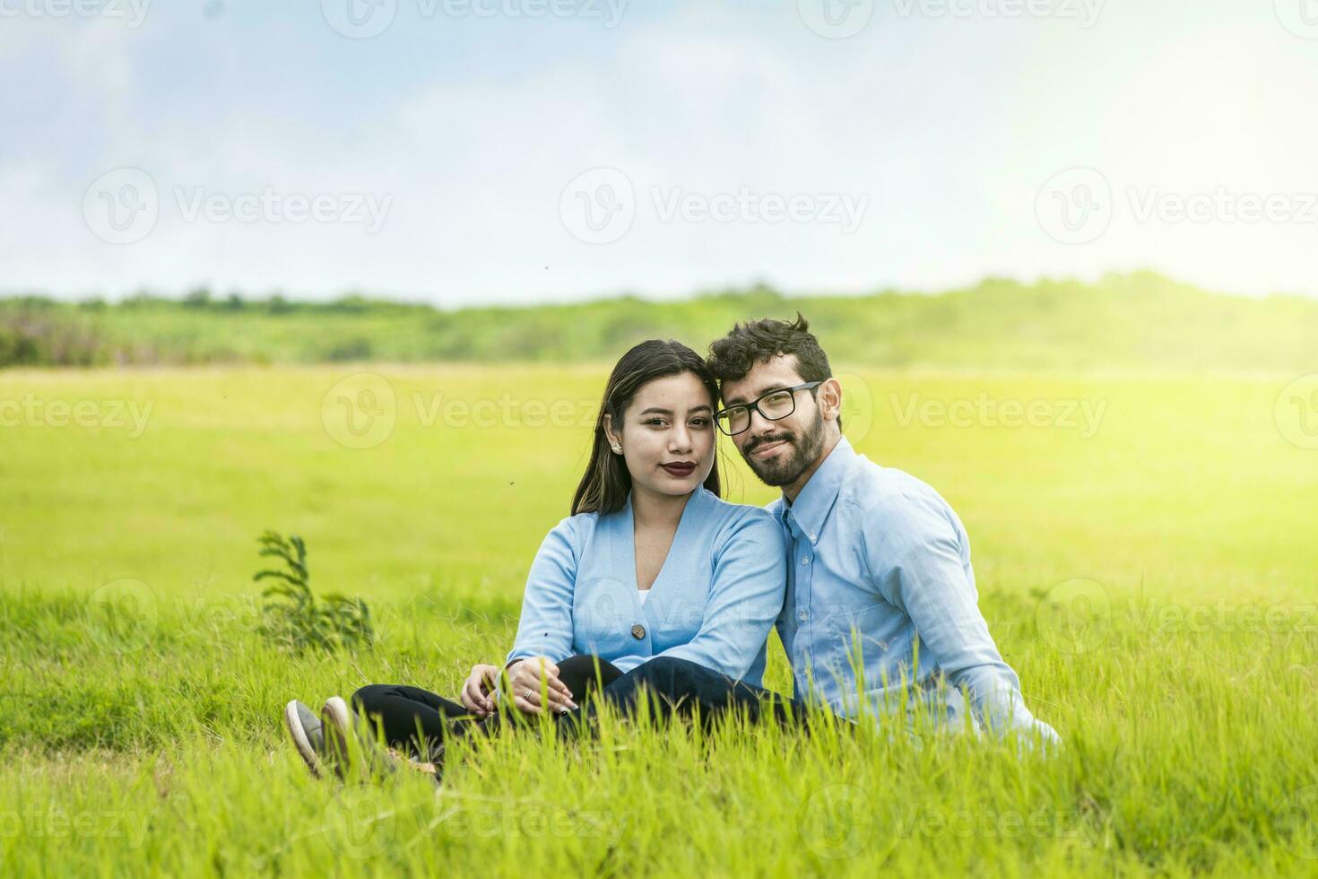 Portrait of a couple in love sitting on the grass in the field, Romantic couple sitting on the grass looking at the camera, Two lovers sitting on the grass looking at the camera photo