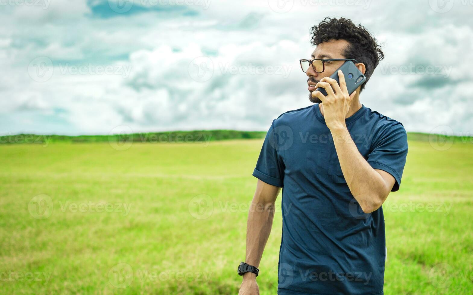 Handsome man calling on the phone in the field. man on the road talking on the phone, person in the field calling on the phone, young man talking on the phone in the field looking to the side photo
