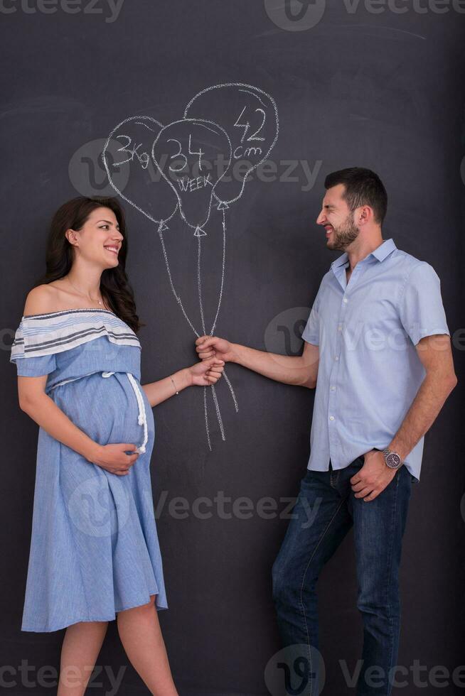 pregnant couple drawing their imaginations on chalk board photo