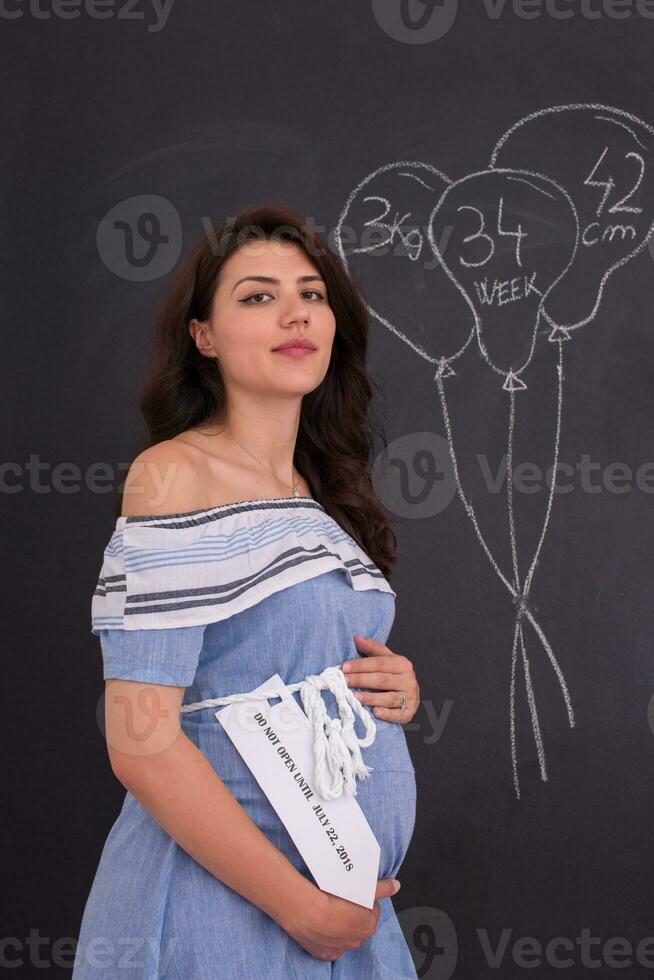 Portrait of pregnant woman in front of black chalkboard photo