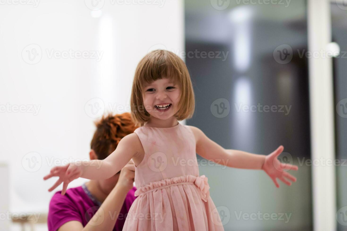 young mother helping daughter while putting on a dress photo