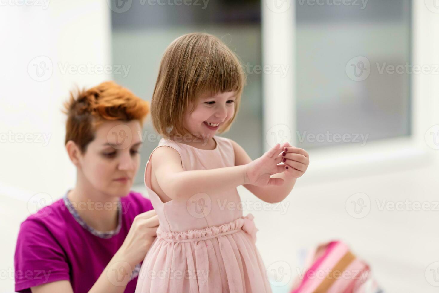 young mother helping daughter while putting on a dress photo