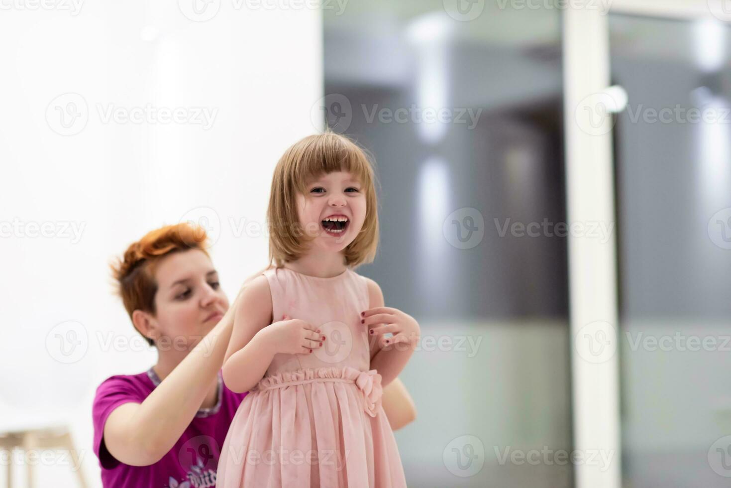 young mother helping daughter while putting on a dress photo