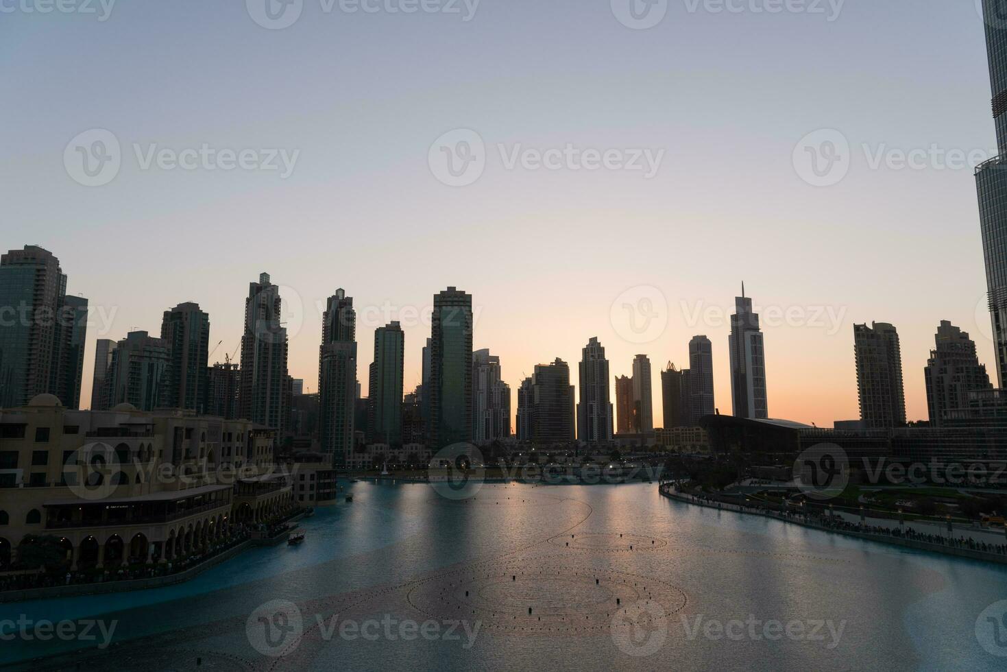 Dubai singing fountains at night lake view between skyscrapers. City skyline in dusk modern architecture in UAE capital downtown. photo