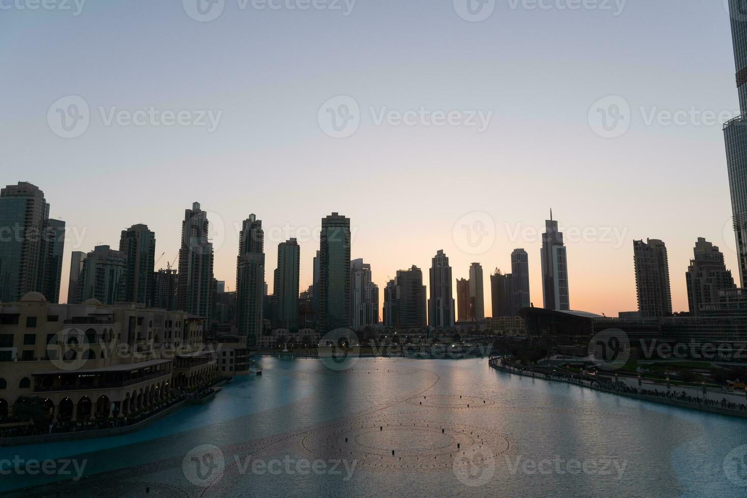 Dubai singing fountains at night lake view between skyscrapers. City skyline in dusk modern architecture in UAE capital downtown. photo
