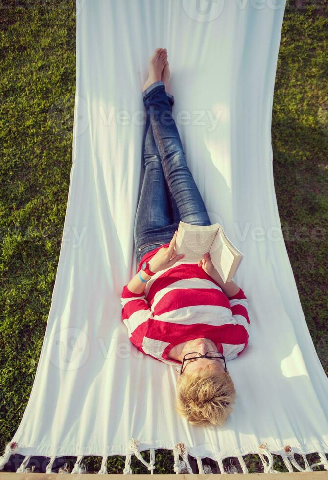 woman reading a book while relaxing on hammock photo