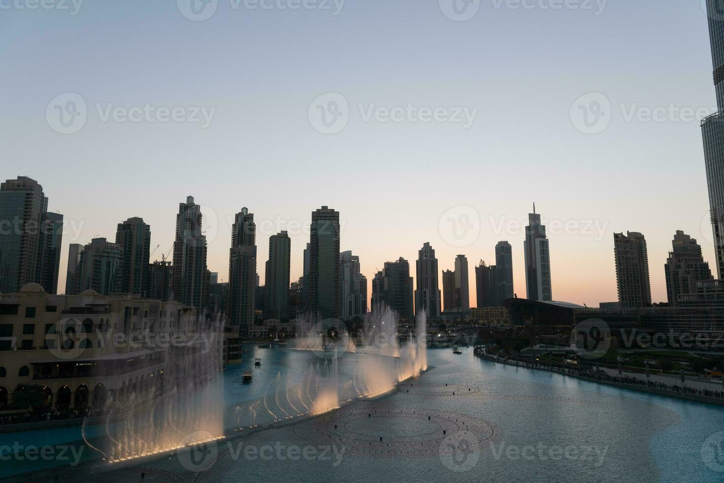 Dubai singing fountains at night lake view between skyscrapers. City skyline in dusk modern architecture in UAE capital downtown. photo