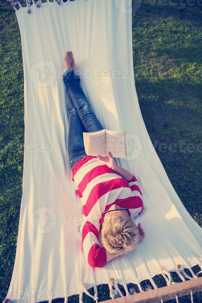 woman reading a book while relaxing on hammock photo