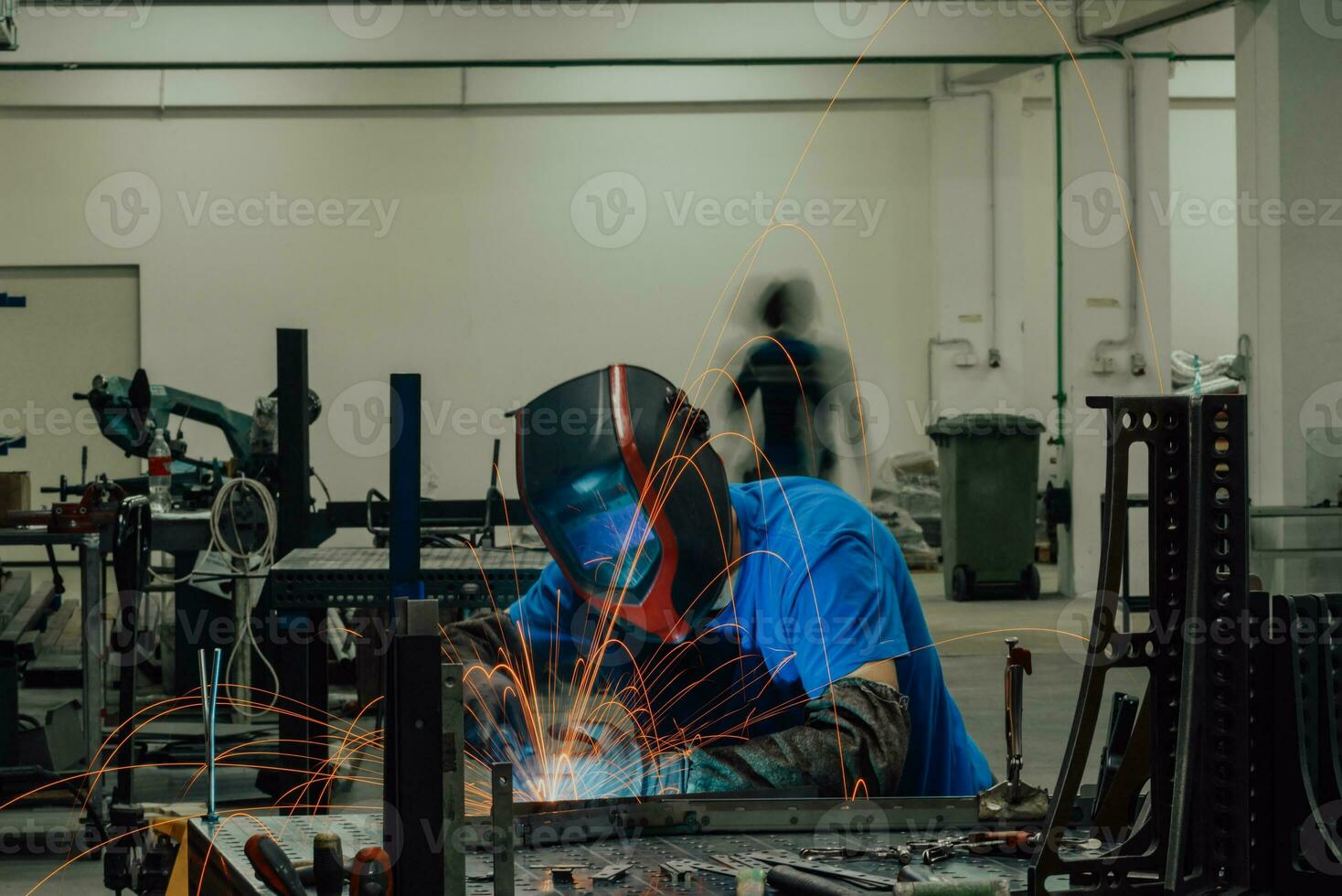 soldador profesional de la industria pesada que trabaja dentro de la fábrica, usa casco y comienza a soldar. enfoque selectivo foto