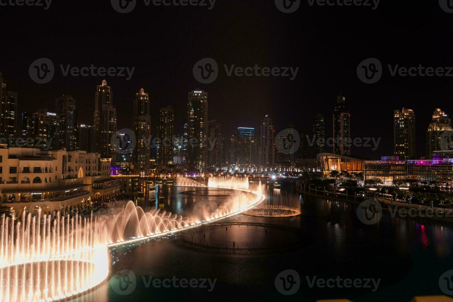 Dubai singing fountains at night lake view between skyscrapers. City skyline in dusk modern architecture in UAE capital downtown. photo