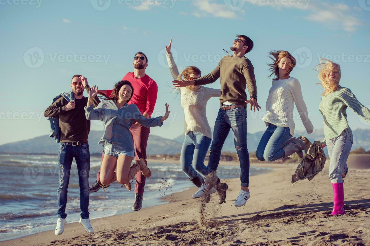young friends jumping together at autumn beach photo