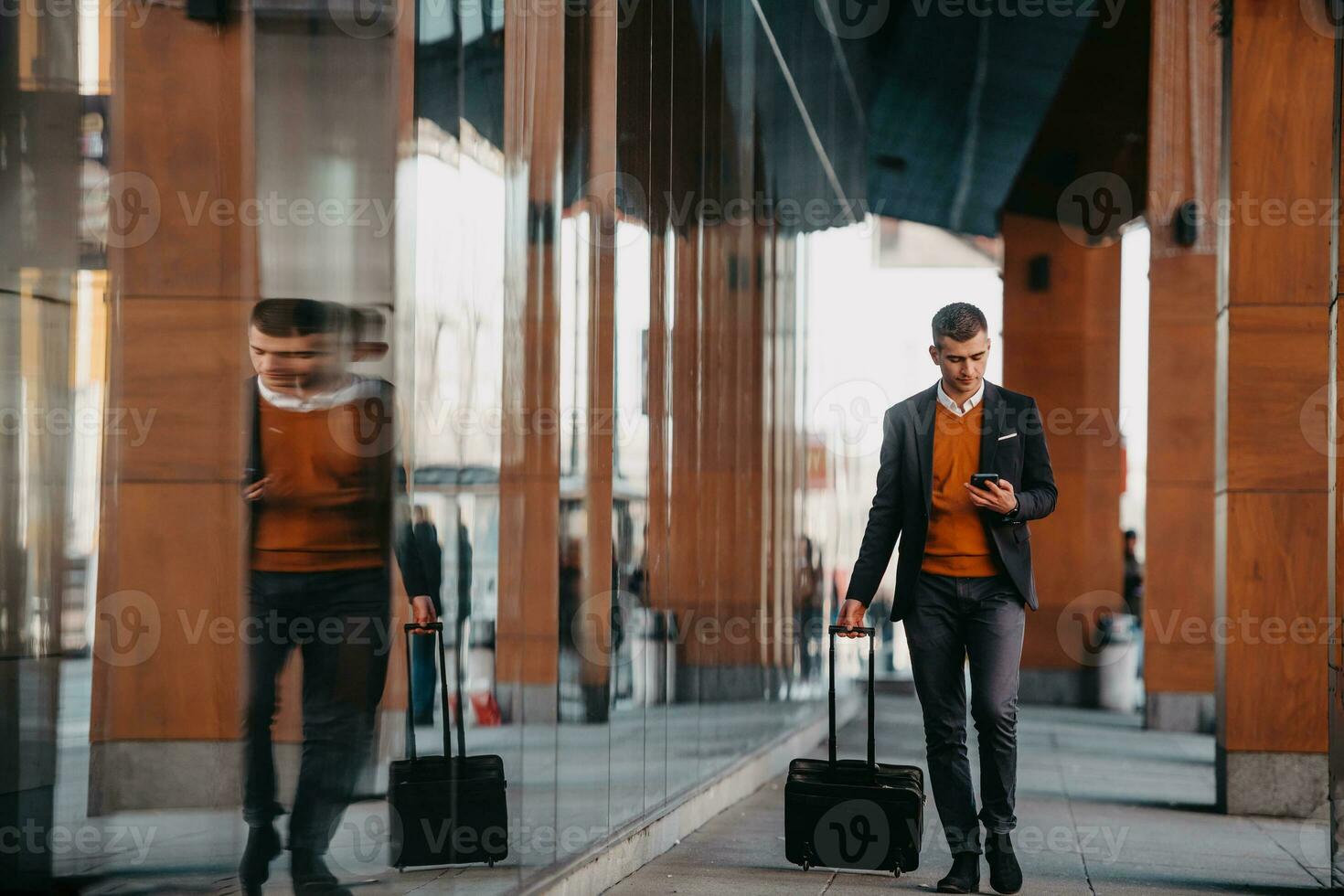 ir a la terminal del aeropuerto. viajero de negocios confiado caminando por las calles de la ciudad y tirando de su maleta bebiendo café y hablando en el teléfono inteligente foto