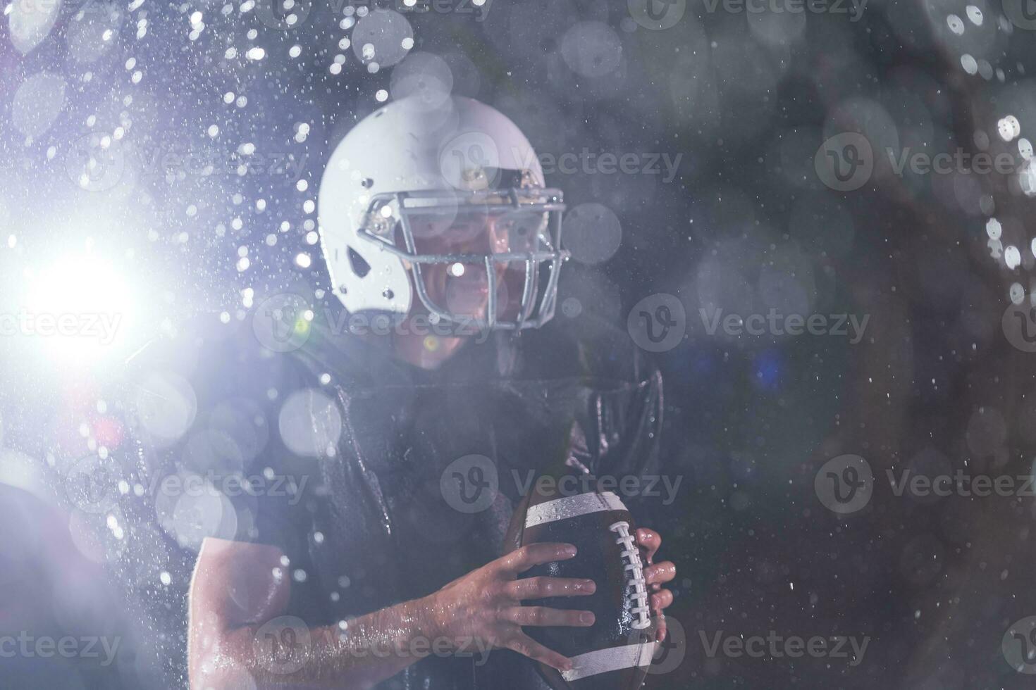 americano fútbol americano campo solitario atleta guerrero en pie en un campo sostiene su casco y Listo a jugar. jugador preparando a correr, ataque y Puntuación aterrizaje. lluvioso noche con dramático niebla, azul ligero foto