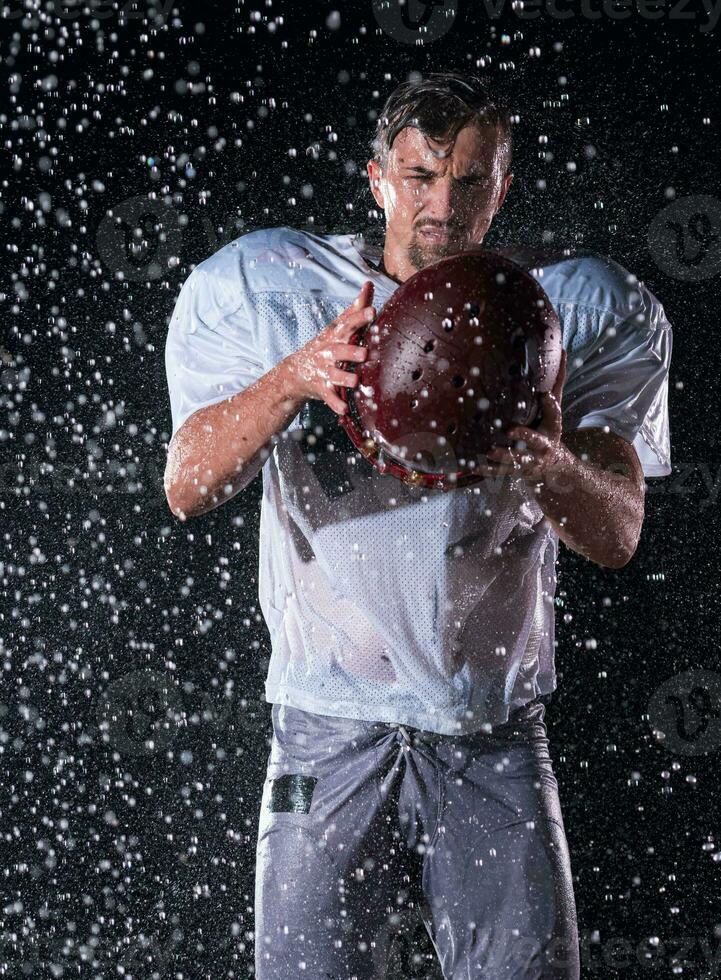 American Football Field Lonely Athlete Warrior Standing on a Field Holds his Helmet and Ready to Play. Player Preparing to Run, Attack and Score Touchdown. Rainy Night with Dramatic Fog, Blue Light photo