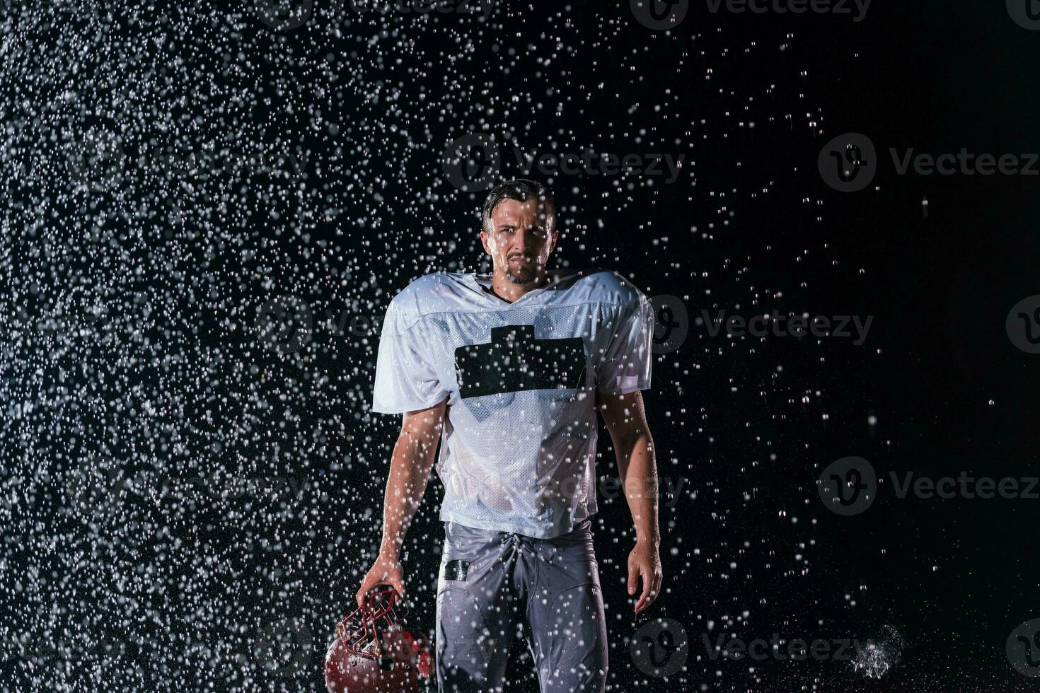 American Football Field Lonely Athlete Warrior Standing on a Field Holds his Helmet and Ready to Play. Player Preparing to Run, Attack and Score Touchdown. Rainy Night with Dramatic Fog, Blue Light photo