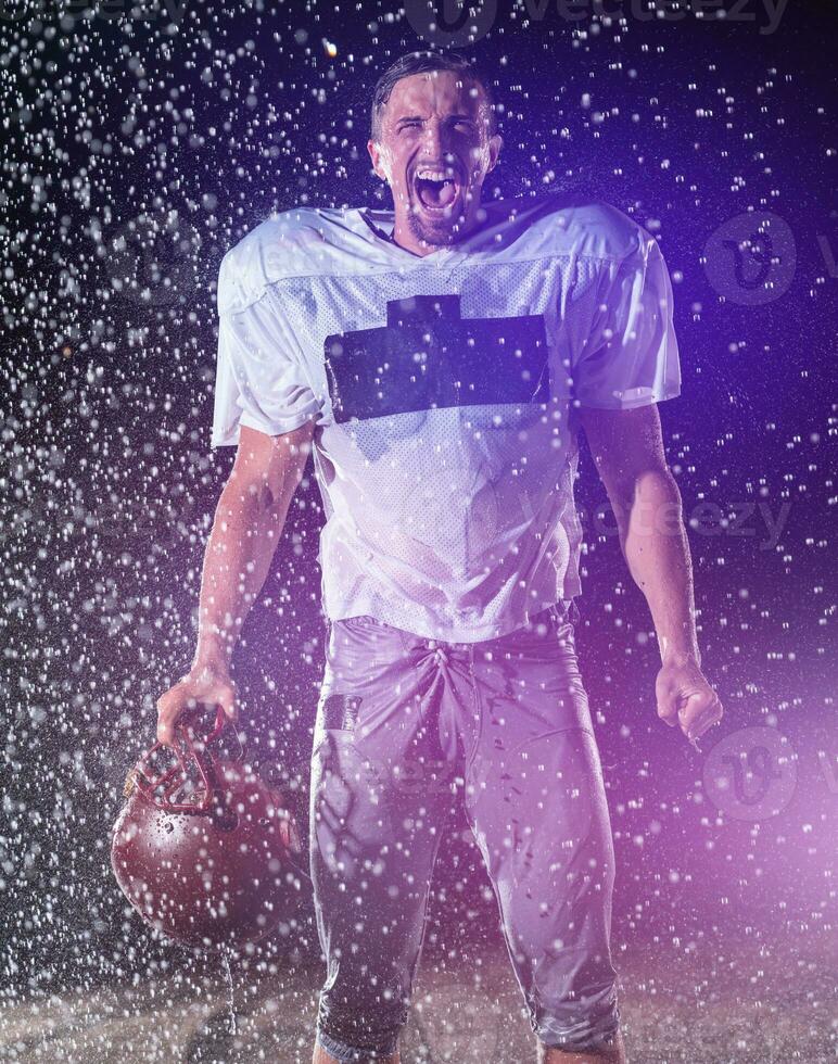 American Football Field Lonely Athlete Warrior Standing on a Field Holds his Helmet and Ready to Play. Player Preparing to Run, Attack and Score Touchdown. Rainy Night with Dramatic Fog, Blue Light photo