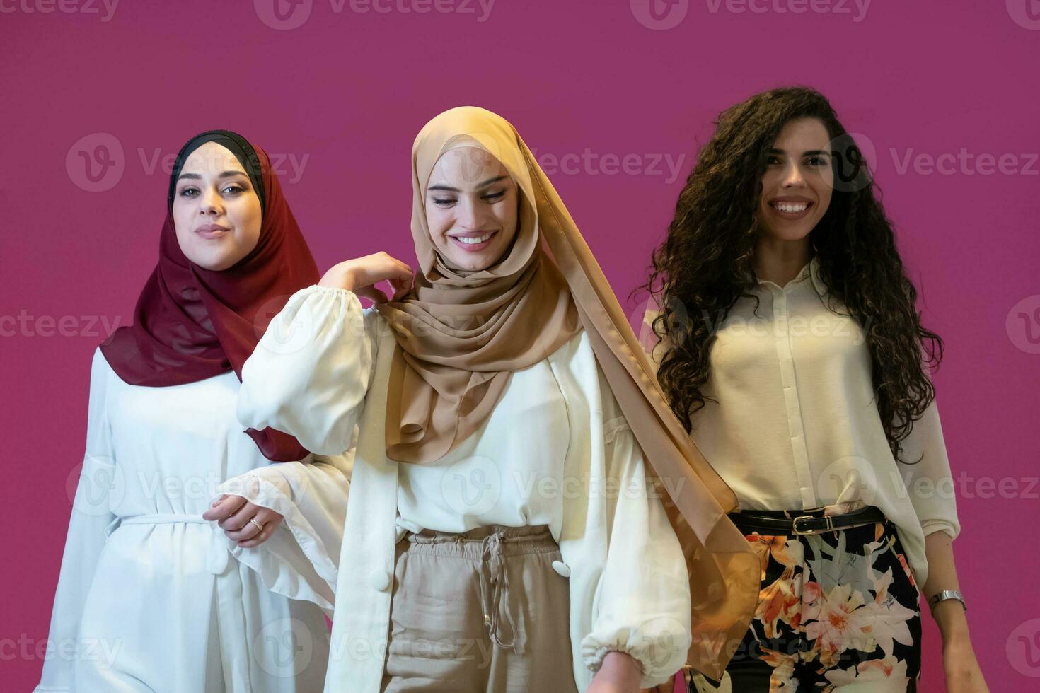 Group portrait of beautiful muslim women two of them in fashionable dress with hijab isolated on pink background representing modern islam fashion and ramadan kareem concept photo