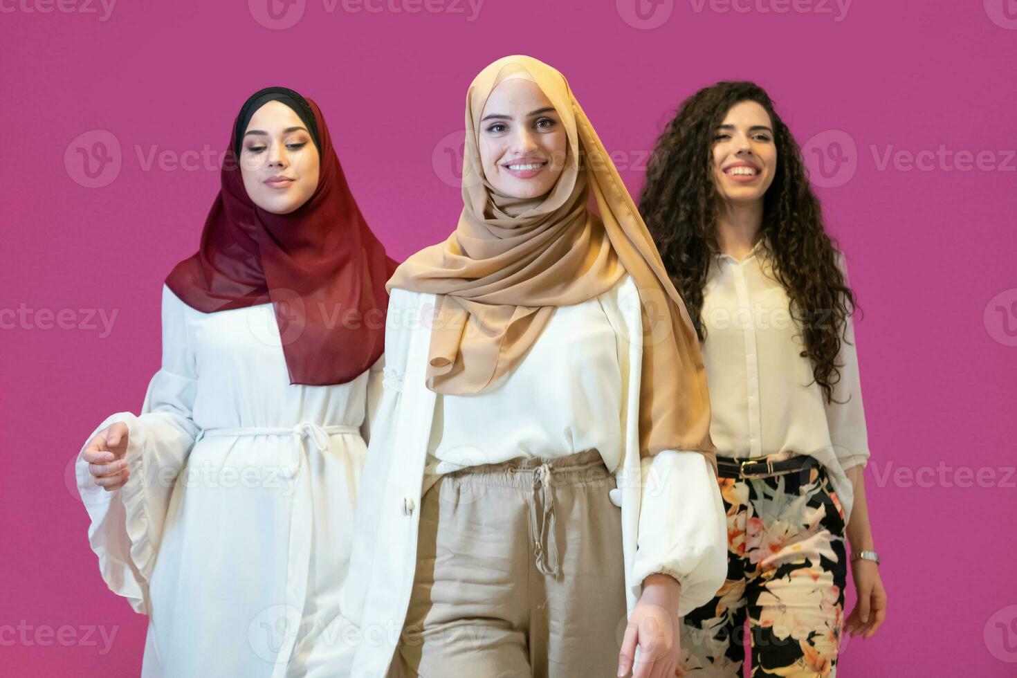 Group portrait of beautiful muslim women two of them in fashionable dress with hijab isolated on pink background representing modern islam fashion and ramadan kareem concept photo