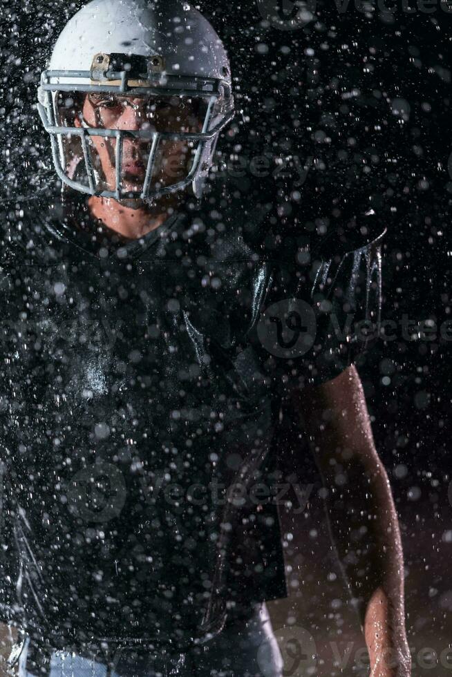 American Football Field Lonely Athlete Warrior Standing on a Field Holds his Helmet and Ready to Play. Player Preparing to Run, Attack and Score Touchdown. Rainy Night with Dramatic Fog, Blue Light photo