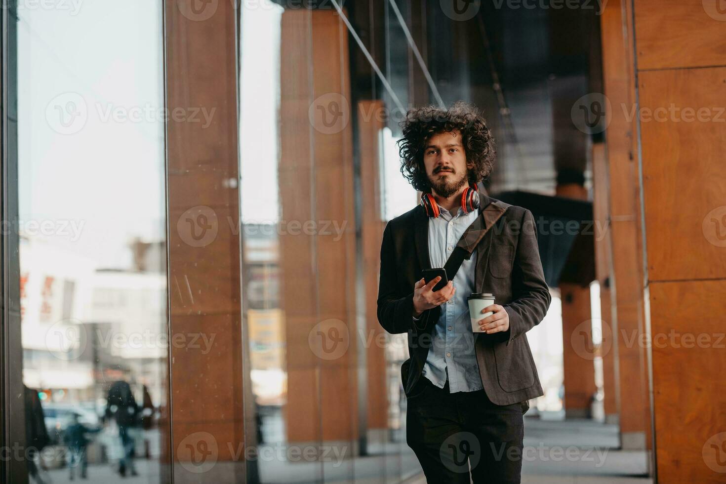 Trendy businessman with leather briefcase in financial district using smartphone while listening audio songs headphones drinking coffee photo