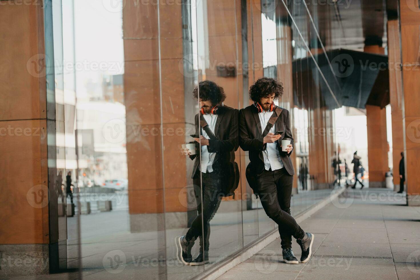 Trendy businessman with leather briefcase in financial district using smartphone while listening audio songs headphones drinking coffee photo