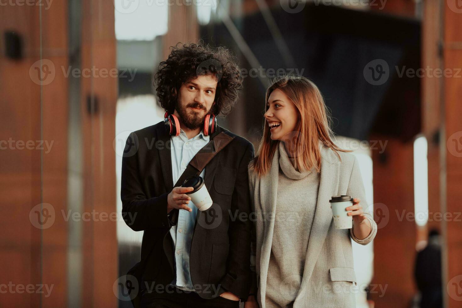 two people on a break from work walk in front of a modern company where they work and drink coffee. photo