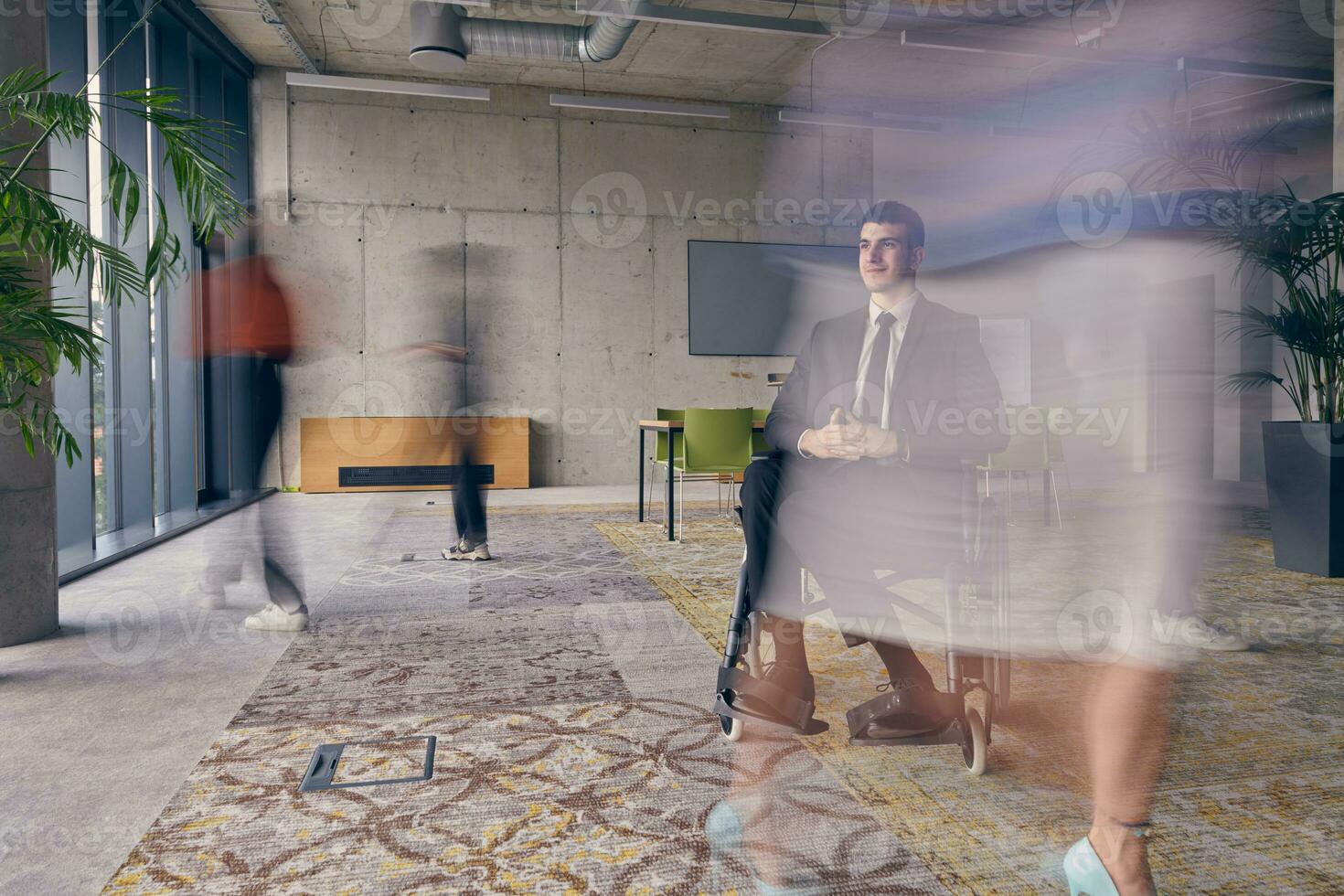 A businessman in a wheelchair in a modern office, surrounded by his colleagues who are portrayed with blurred movements, symbolizing their support and solidarity as they navigate the workspace together. photo