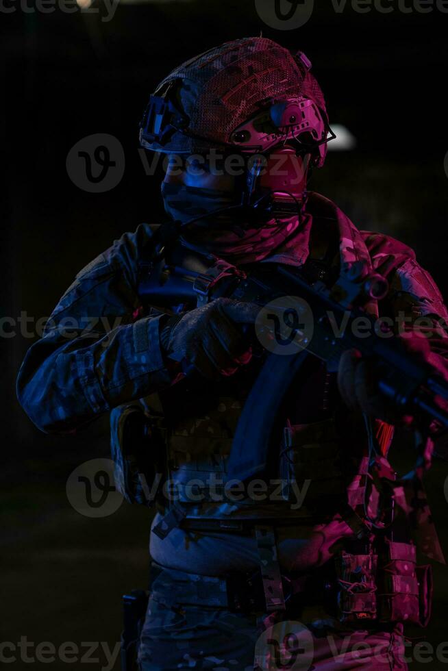 Ejército soldado en combate uniformes con un asalto rifle y combate casco noche misión oscuro antecedentes. azul y púrpura gel ligero efecto. foto