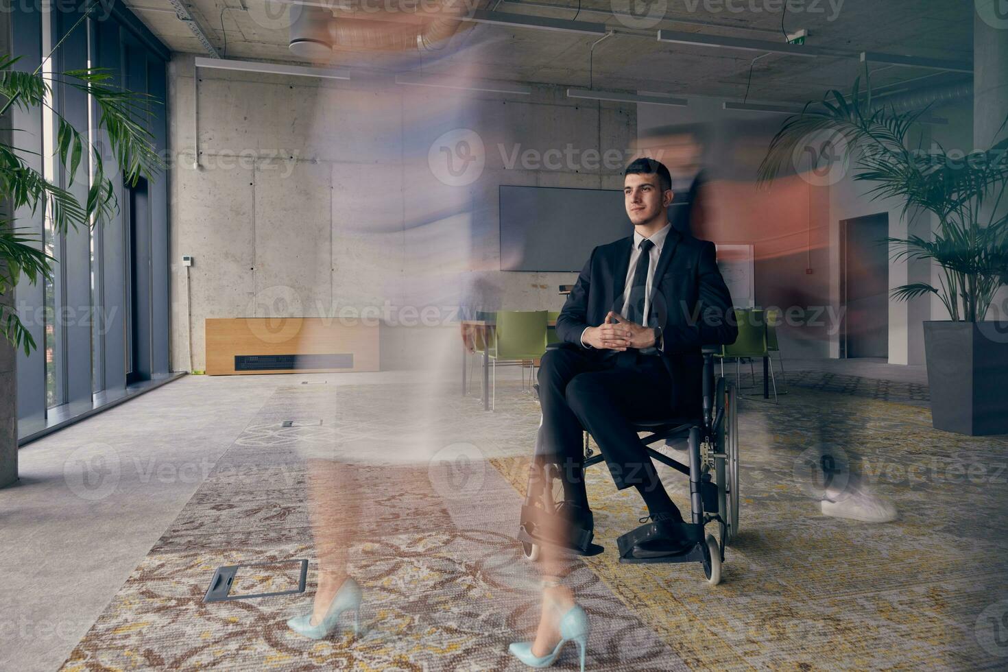A businessman in a wheelchair in a modern office, surrounded by his colleagues who are portrayed with blurred movements, symbolizing their support and solidarity as they navigate the workspace together. photo