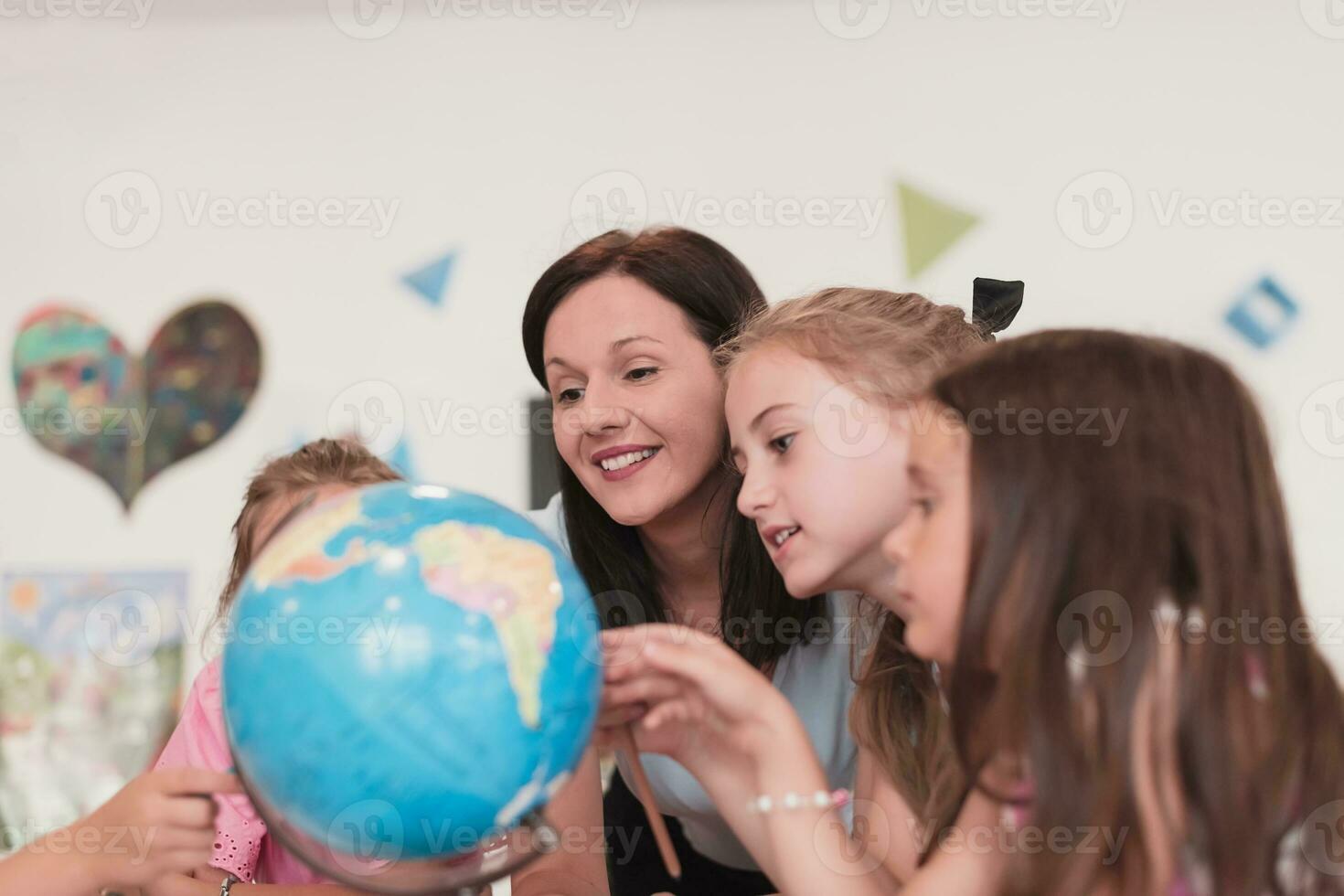 Female teacher with kids in geography class looking at globe. Side view of group of diverse happy school kids with globe in classroom at school. photo