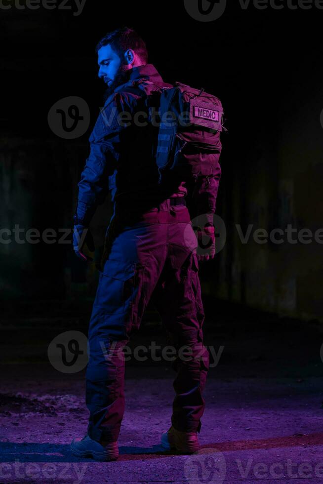 Ejército soldado en combate uniformes con un asalto rifle y combate casco noche misión oscuro antecedentes. azul y púrpura gel ligero efecto. foto