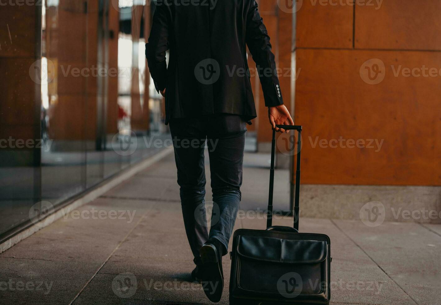 Going to airport terminal. Confident businessman traveler walking on city streets and pulling his suitcase drinking coffee and speaking on smartphone photo