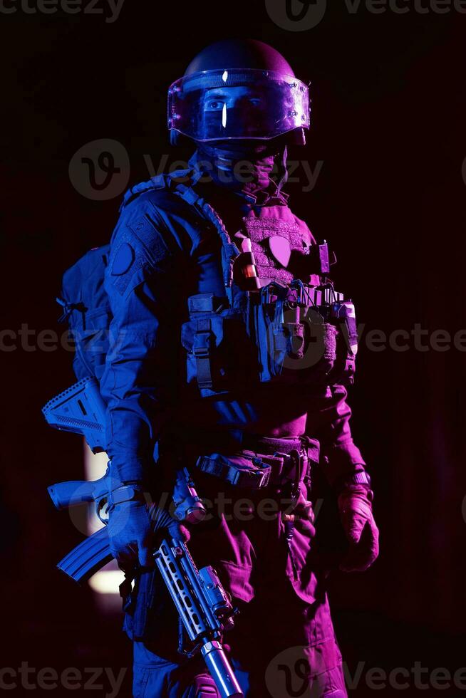 Ejército soldado en combate uniformes con un asalto rifle y combate casco noche misión oscuro antecedentes. azul y púrpura gel ligero efecto. foto